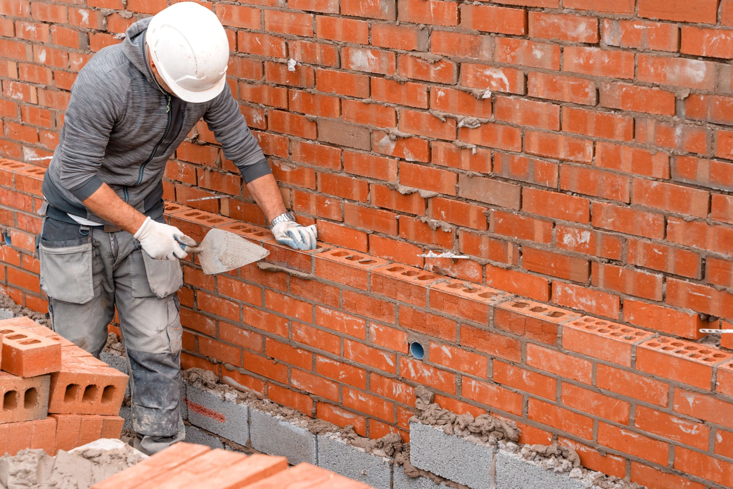 Stone Haven Developments A construction worker wearing a helmet and gloves uses a trowel to lay bricks and apply mortar on a brick wall under construction for Stone Haven Developments. Ontario