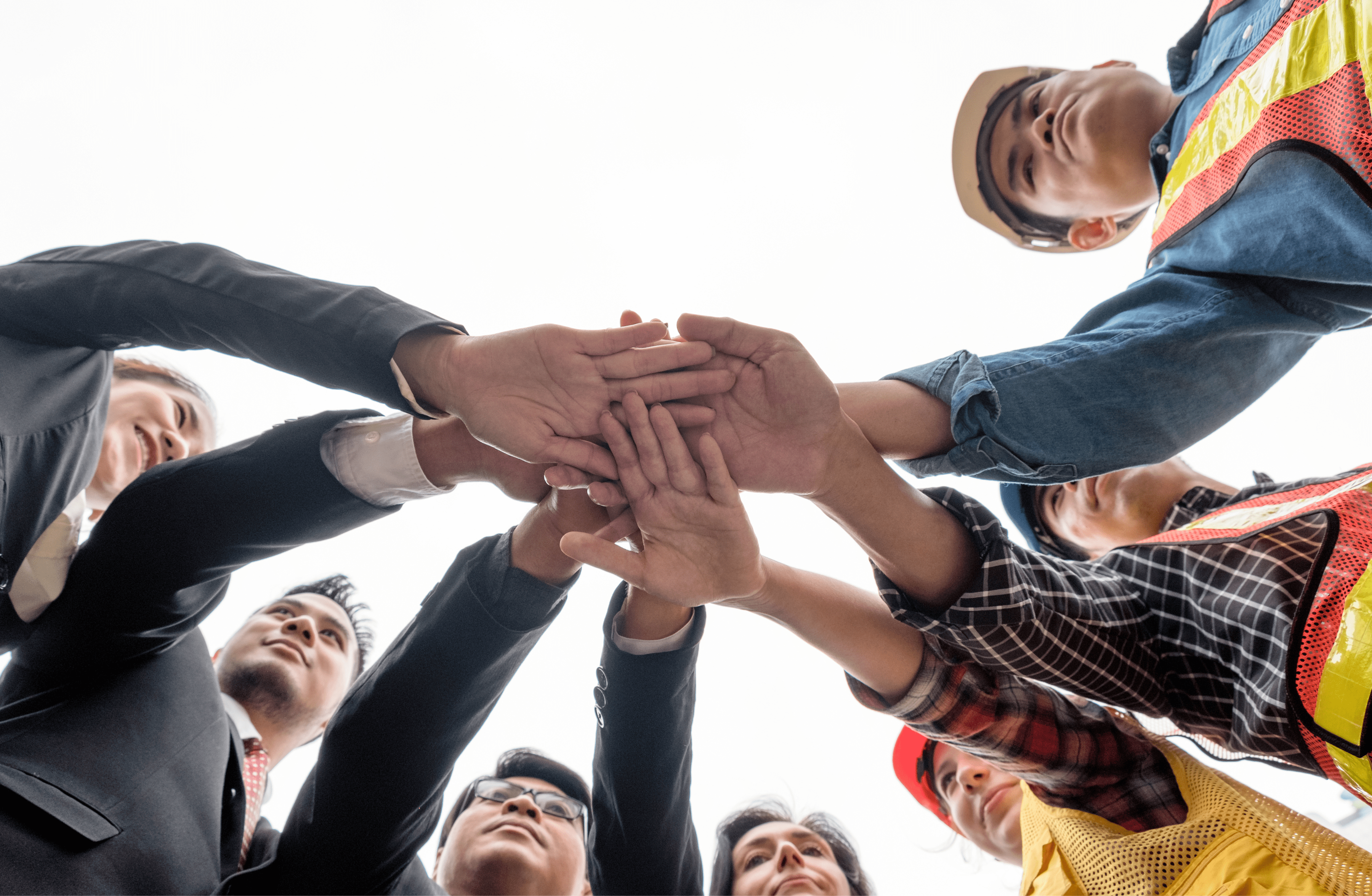 Stone Haven Developments A diverse group of professionals in business and construction attire stand in a circle, stacking their hands together in a gesture of teamwork and unity at Stone Haven Developments. Ontario