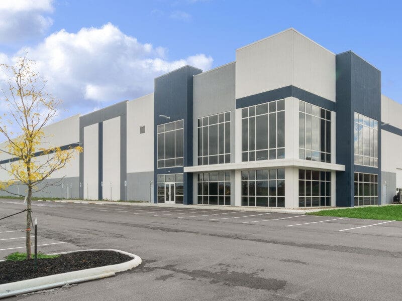 Stone Haven Developments Modern industrial warehouse building by Stone Haven Developments, featuring large glass windows, a gray and white facade, and an empty parking lot under a partly cloudy sky. Ontario
