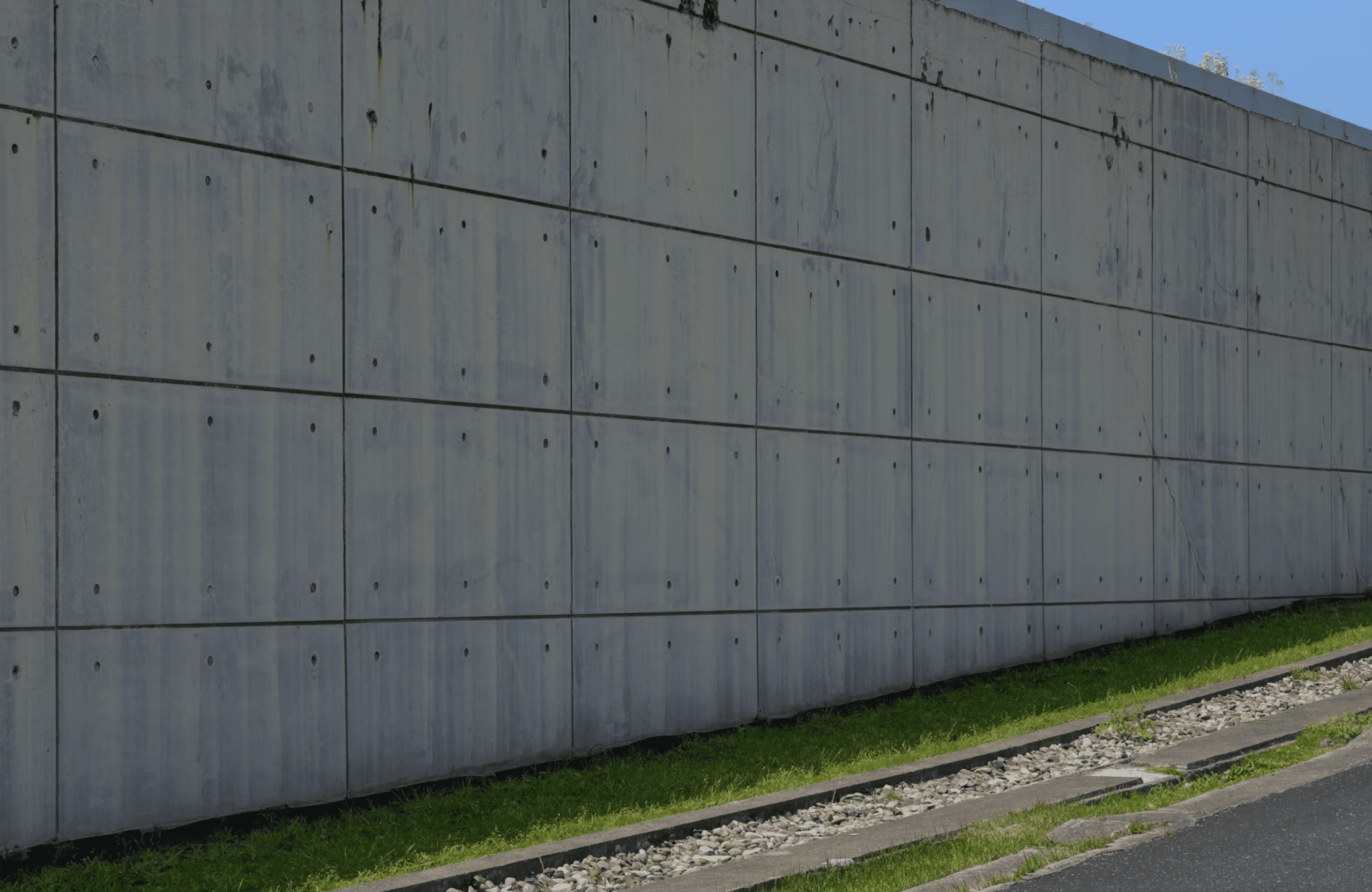 Stone Haven Developments A large concrete wall with visible panel lines runs alongside railroad tracks and a strip of green grass under a clear blue sky. Ontario