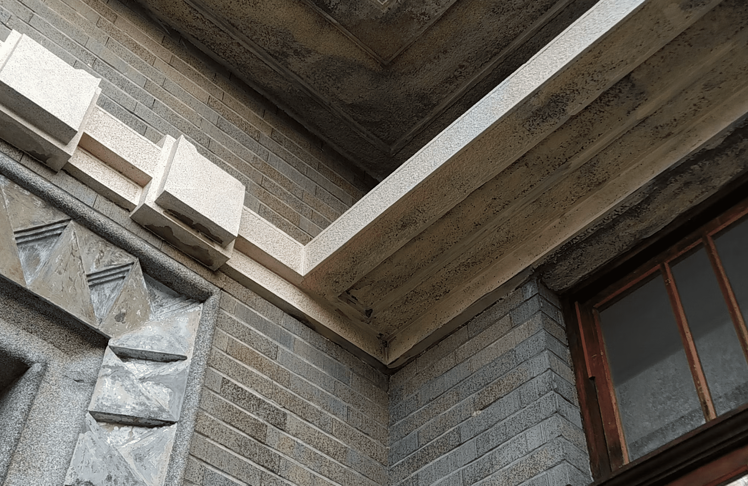 Stone Haven Developments Close-up of a building corner showing textured grey brick walls, a section of a window with a wooden frame, and geometric stone details near the ceiling. Ontario