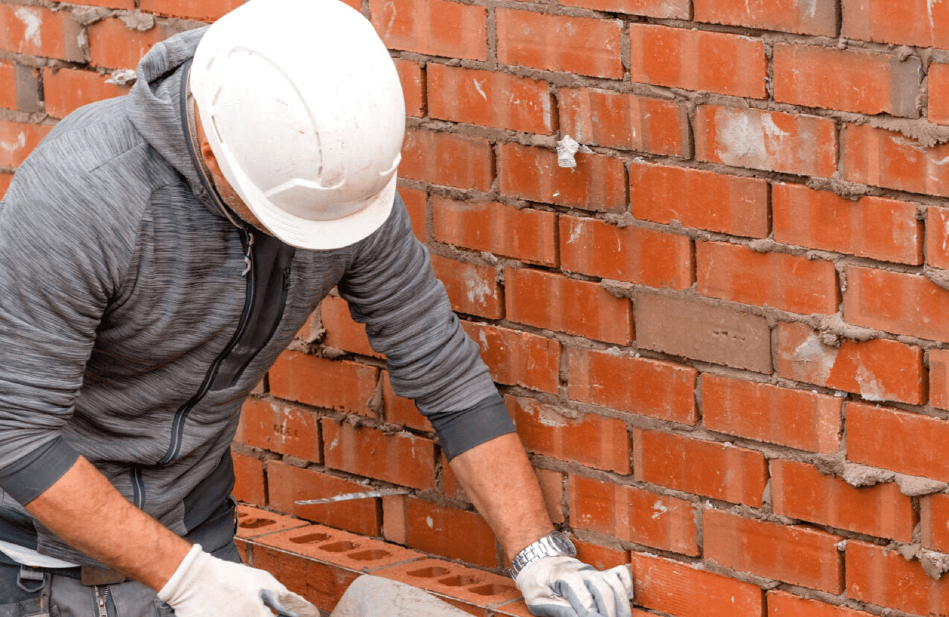 Stone Haven Developments A construction worker in a white hard hat and gloves lays bricks while building a brick wall. Ontario