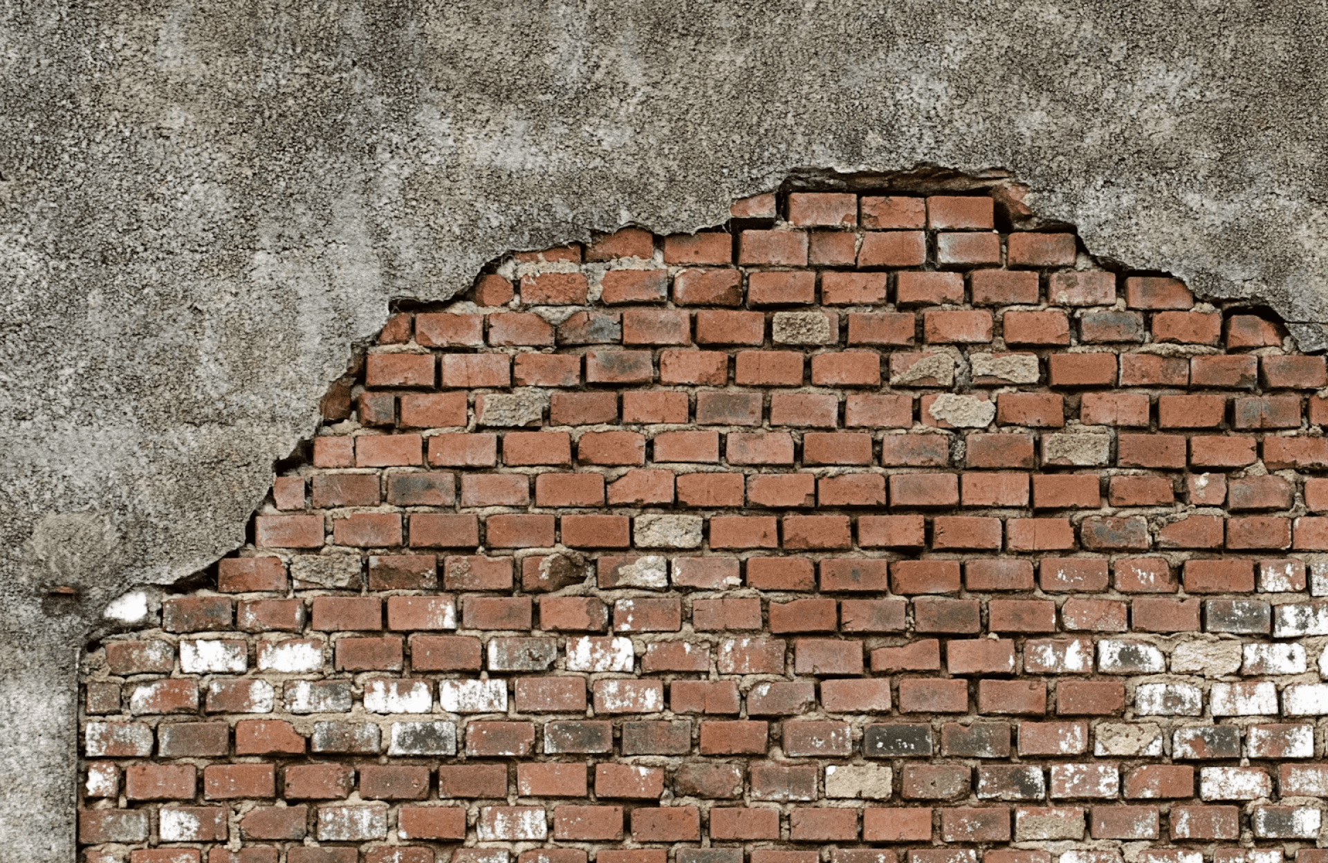 Stone Haven Developments A partially exposed brick wall with irregular edges, showing red bricks beneath a layer of worn gray plaster. Ontario