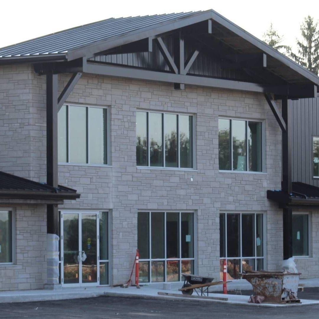 Stone Haven Developments Modern two-story commercial building with stone and metal exterior, large windows, and construction equipment and caution signs in front. Ontario